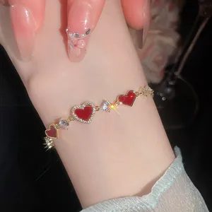 Detailansicht eines 14k vergoldeten Armbands mit roten Herzen und Zirkonia am Handgelenk.