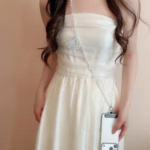 Détail d'une élégante lanière de téléphone en perles et cristaux sur une robe blanche
