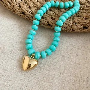 Dettaglio di una collana di perle acriliche turchesi venate con pendente a cuore dorato
