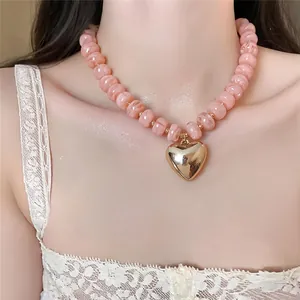 Dettaglio di un'elegante collana di perle acriliche rosa con ciondolo a cuore dorato