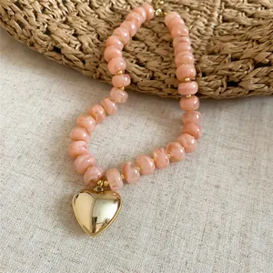 Dettaglio di perle acriliche marmorizzate rosa e pendente cuore in finitura oro