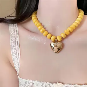 Vista dettagliata della collana di perle acriliche gialle con grande ciondolo a cuore dorato su modella