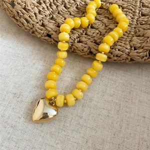 Vista dettagliata delle perle in acrilico giallo e di un ciondolo a cuore in oro lucido.