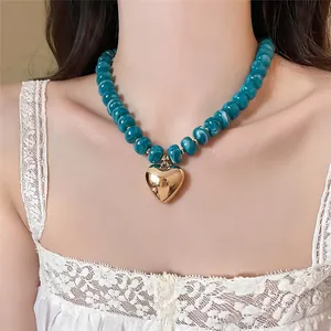 Dettaglio ravvicinato di una collana di perle acriliche blu con pendente a cuore d'oro
