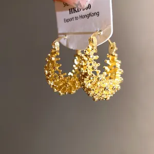 Close-up of golden French hollow flower basket hoop earrings with intricate texture.