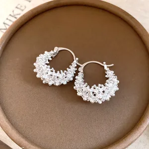 Close-up of French silver hollow flower basket earrings with textured detail on brown base