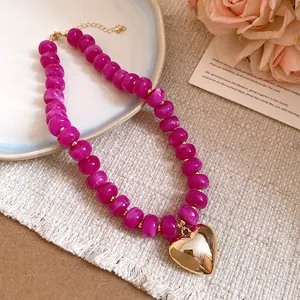 Close-up of fuchsia resin beaded necklace with a polished gold heart pendant detail