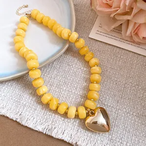 Detail view of a vibrant yellow resin beaded necklace with a gold heart pendant on a linen fabric.