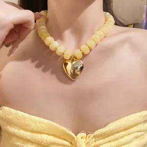 Detailed view of a yellow resin beaded necklace with a polished gold heart pendant on a model