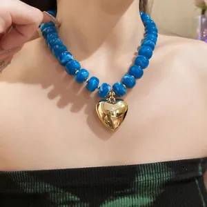 Close-up view of a blue resin bead necklace with a gold heart pendant on a model.