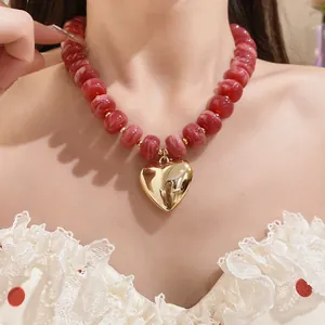 Detail shot of a red resin beaded necklace featuring a large polished gold heart pendant