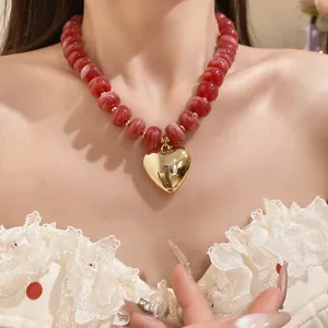 Close-up view of a pink marbled resin beaded necklace with a gold heart pendant on a model