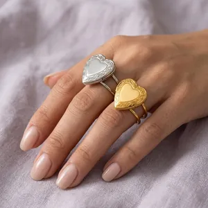 Elegant hand wearing stainless steel gold and silver heart locket rings on soft fabric