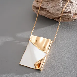 Close-up of gold book flip pendant necklace with white enamel dripping oil detail