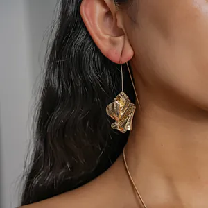 Close-up detail of a gold crumpled metal book-inspired earring on an Asian model