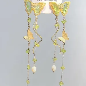 Detailed view of long gold butterfly dangle earrings with green stones and pearl drops