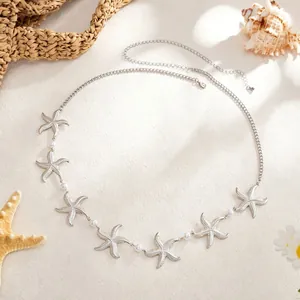 Silver starfish body chain with white pearls on beach theme background detail view