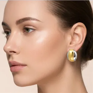 Gros plan d'élégantes boucles d'oreilles irrégulières bicolores or et argent sur modèle.