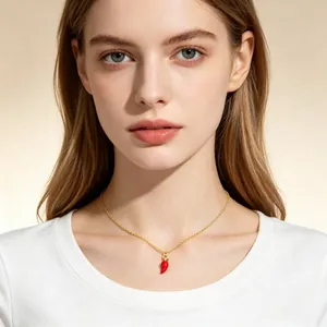 Détail d'un collier avec un petit pendentif piment rouge sur une chaîne dorée fine.