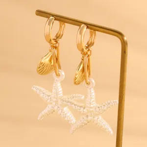 Gros plan sur les boucles d'oreilles pendantes étoile de mer et coquillage en métal doré