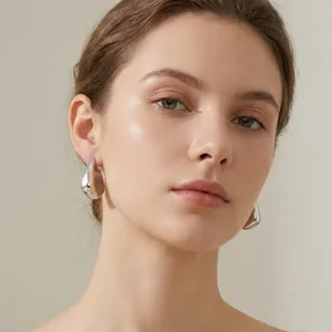Gros plan d'un modèle portant des boucles d'oreilles irrégulières en forme de nageoire argentée