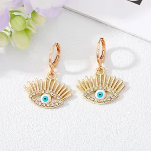 Vue détaillée de boucles d'oreilles dorées œil protecteur avec des cils en strass