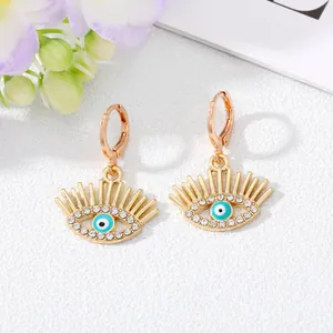 Vue détaillée de boucles d'oreilles œil porte-bonheur dorées avec cils et cristaux.