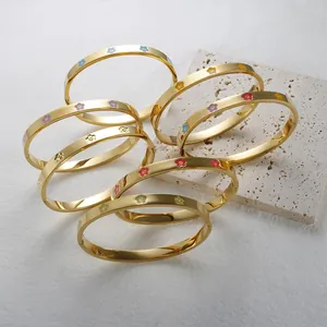 Macro view of multiple colorful enamel plum blossom gold-plated stainless steel bangles.
