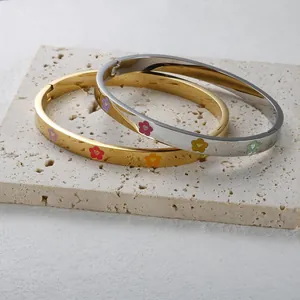 Close-up of gold and silver stainless steel bangles with colorful enamel flower patterns.