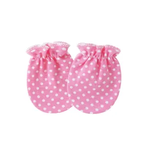 Close-up detail of pink newborn baby mittens with white polka dots and elastic cuffs.