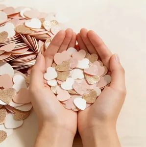 Hands holding glitter gold and pink heart-shaped confetti for Valentine's Day decoration