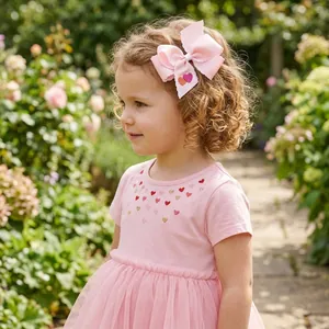 Handmade pink ribbon bow hair clip with heart detail worn by a little girl in garden