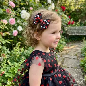 Close-up of a handmade heart patterned bow hair clip worn by a little girl in a garden