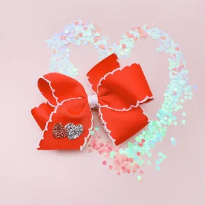 Red polyester hair bow with scalloped white edges and glittery heart detail for girls