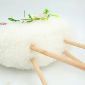Macro detail of pastoral white sherpa lamb doll featuring natural wooden legs and green leaves