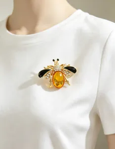 Detailed close-up of a gold honeybee brooch with amber stone pinned to a white shirt