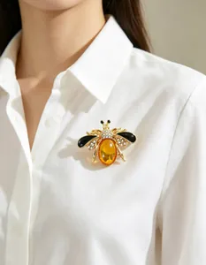 Detailed view of an elegant bee brooch with amber stone and rhinestones on a white shirt