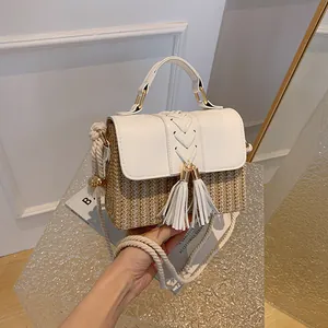 Close-up view of a stylish white straw woven handbag with tassels and rope strap