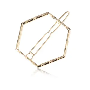 Detailed view of a golden hexagonal hair clip with a twisted texture on a white surface.