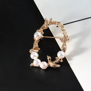 Détail d'une broche en forme de couronne de vigne dorée avec perles et oiseau