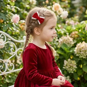 Red velvet bow hair clip with white scalloped edges worn by a young girl in a garden setting