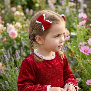 A detailed view of a festive red velvet bow hair clip worn by a young girl in a garden.