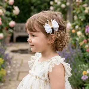 Toddler girl wearing a gold glitter crown bow hair clip accessory in a lush garden.