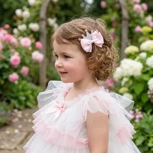 Toddler girl wearing a pink bow hair clip with a silver glitter crown in a garden