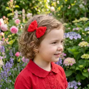 Close-up of a toddler wearing a red lace bow hair clip in a blooming garden setting