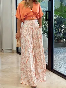 Détail élégant d'un ensemble d'été avec haut à col en V orange et pantalon fleuri.