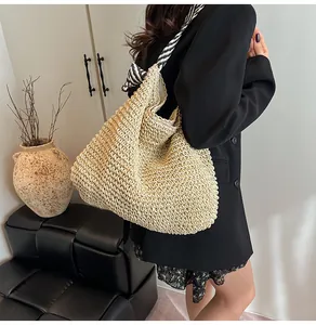 Detailed view of a large beige straw woven tote bag with navy striped shoulder strap