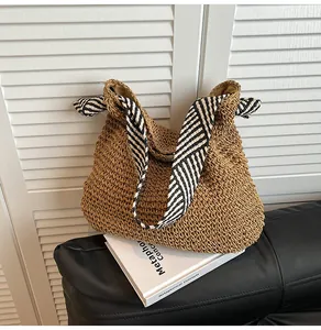 Close-up detail of a woven straw tote bag with black and white striped shoulder straps.