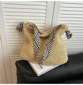 Nautical style straw woven tote bag with striped wide shoulder strap on a book