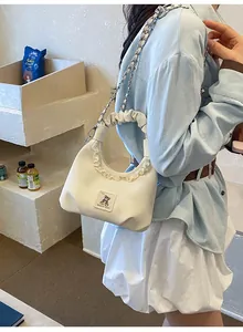 Detailed view of cute white pleated handbag with ruffle trim and bear patch on model.